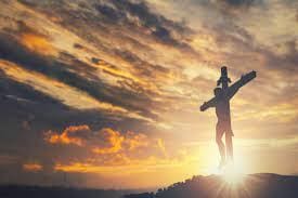 A person standing on top of a hill with a cross.