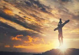 A person standing on top of a hill with a cross.